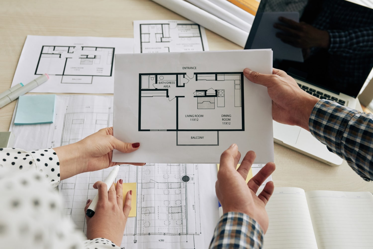 Two professionals discussing house floor plan layouts and architectural blueprints during an interior design planning session.