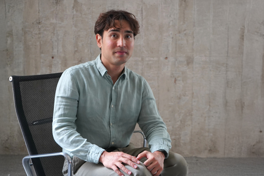 Ethan Ilktan, Architectural Designer at WATG's Los Angeles office, seated in a chair against a concrete wall.